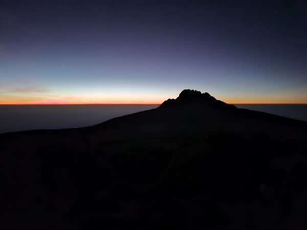Mawenzi Peak in silhouette at dawn from Gilman's Point on Kibo, the sunrise band low on the horizon and the saddle in shadow below. Nelson Mushi, our lead guide, says Mawenzi is the more technically demanding peak to climb in Africa after Mount Kenya.