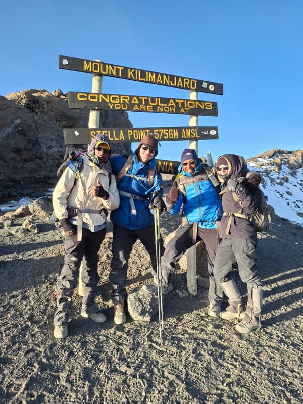 Climbers at the Stella Point signboard on the crater rim, 5,756 m, in the first light after summit night.