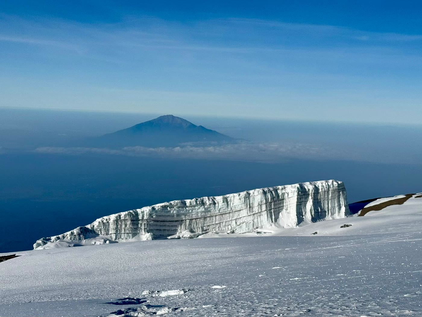 A summit glacier wall on Kilimanjaro with Mount Meru floating above the cloud sea in the distance