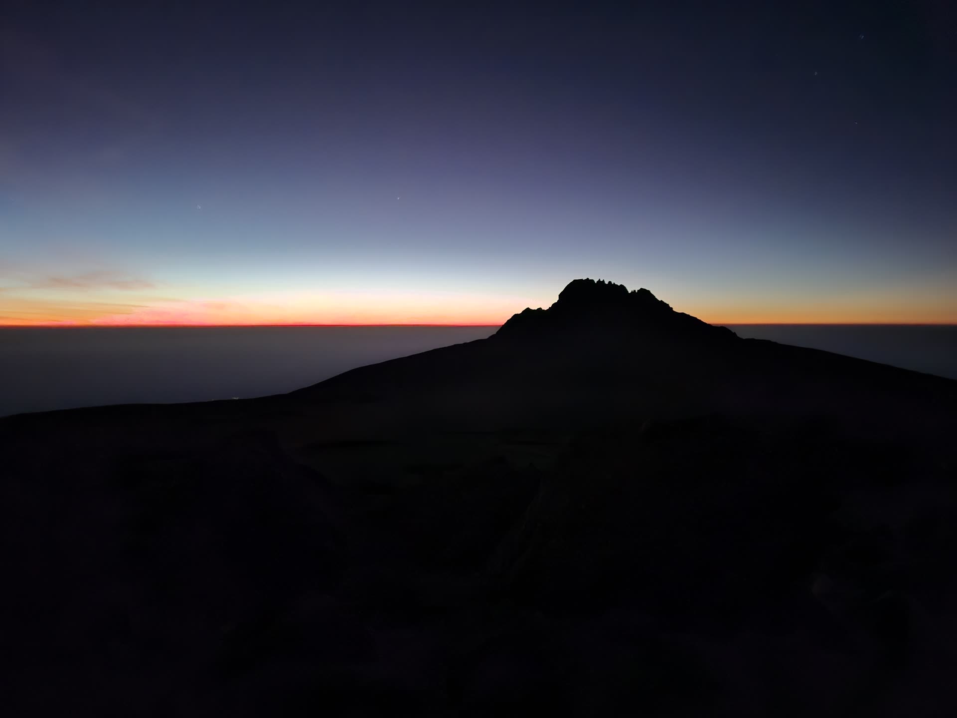 Mawenzi Peak in silhouette at dawn, seen from Gilman's Point on Kibo, the sunrise band low on the horizon and the saddle in shadow below